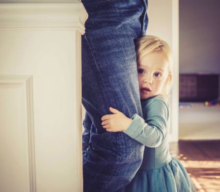 Un enfant se cache derrière son père.