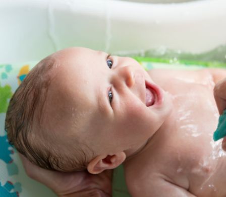 Baby liegt in einer Babywanne und lacht