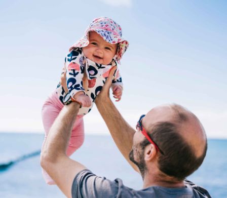 Vater hebt Baby mit Sonnenhut in die Höhe